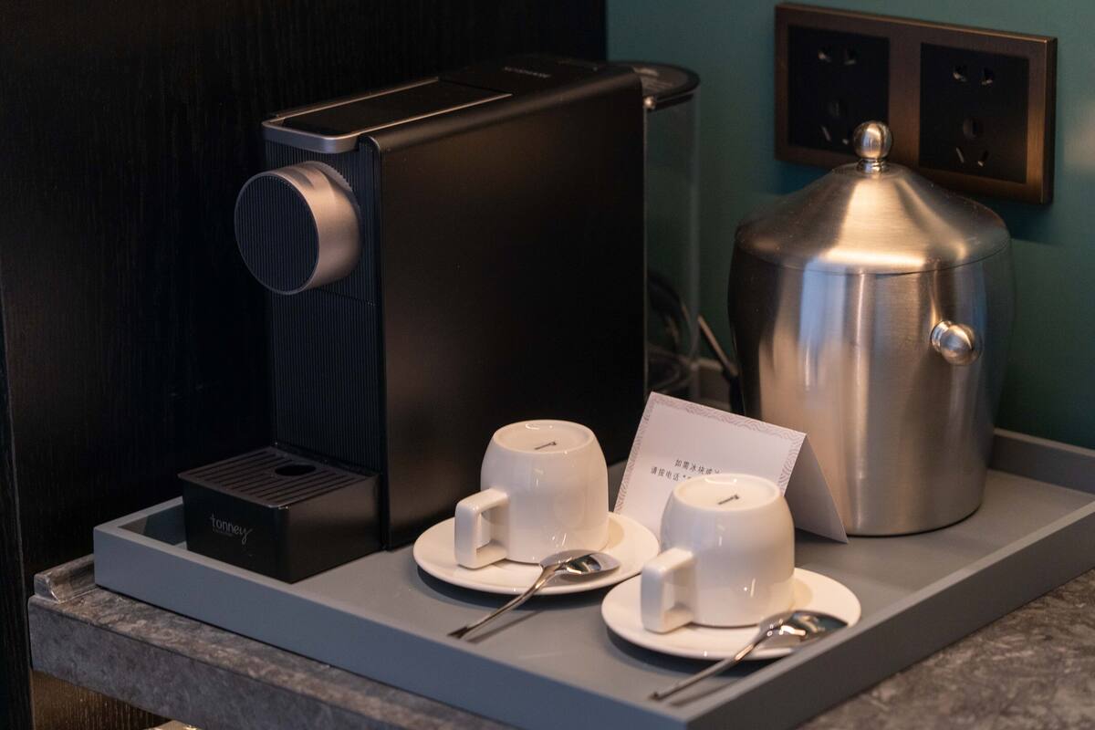 Un coin café comprenant une machine à café, deux tasses, une cuillère et une carte, le tout posé sur un comptoir.