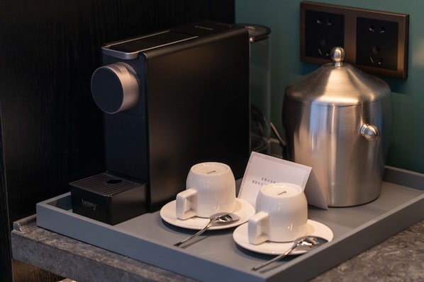 Una estación de café con una cafetera, dos tazas, una cuchara y una tarjeta sobre una encimera.