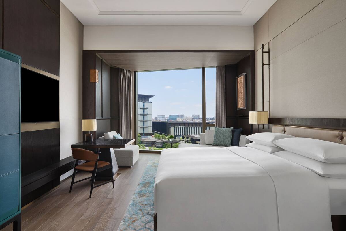 Une chambre d’hôtel moderne dotée d’un grand lit, d’un bureau, d’une chaise et offrant une vue sur le paysage urbain.