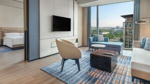 Ein modernes Hotelzimmer mit großem Fenster und Blick auf die Stadt, einem flachbildfernseher an der Wand, einem Sofa, einem Couchtisch und einem Bett mit Kopfteil.