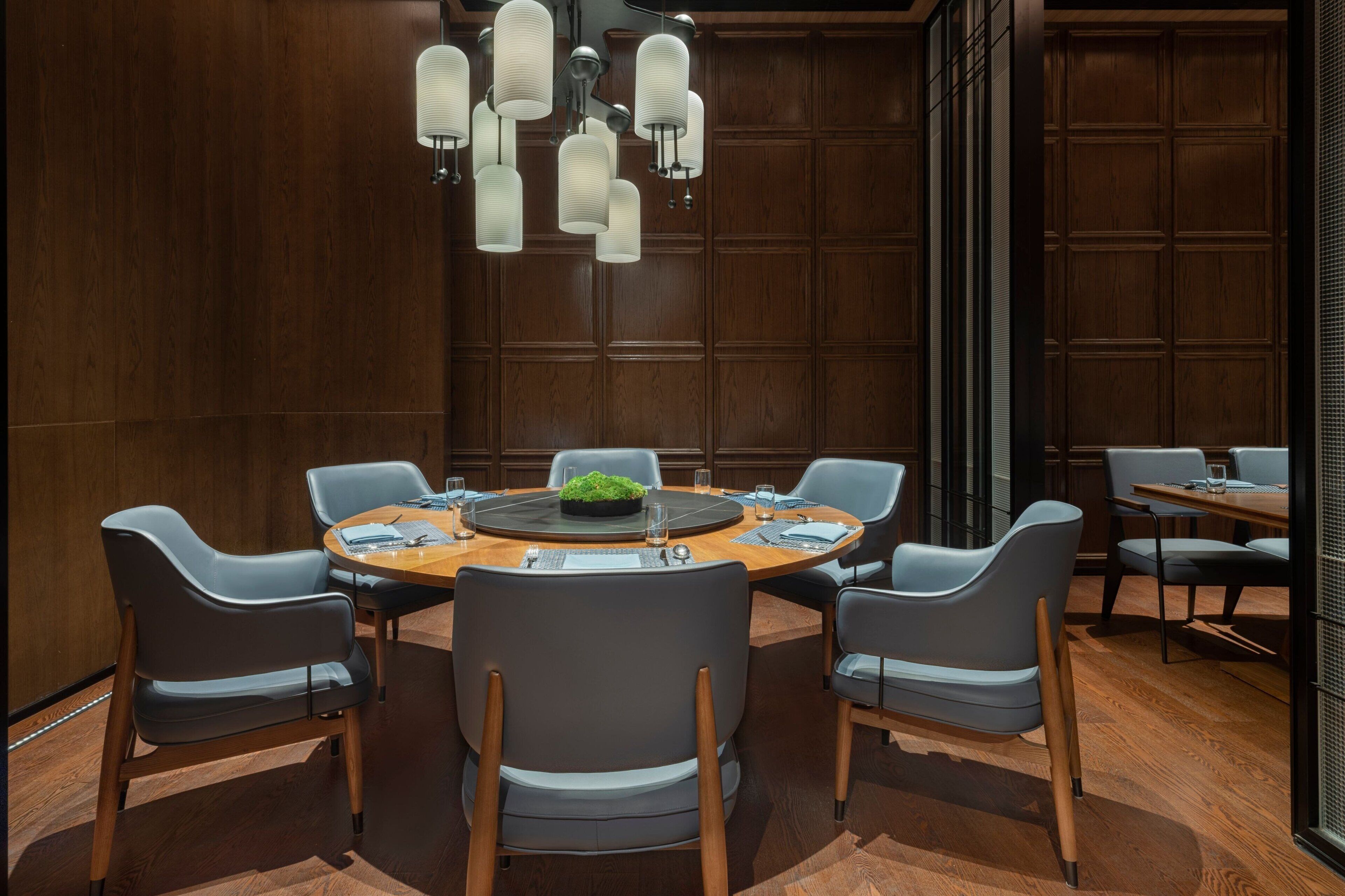 A conference room with a round table, six chairs, and a modern chandelier.