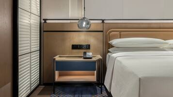 A hotel room with a bed, bedside table, lamp, and a control panel on the wall.