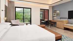 A hotel room with a large bed, a desk, a chair, and a balcony with a view of greenery. - Four Points By Sheraton Hainan, Qiongzhong (Qiongzhong County)