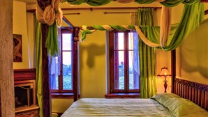 A room with a bed, two windows with curtains, a fireplace, and a lamp. - Archontiko Polyzos 19 Chrysanthemo (Volos)