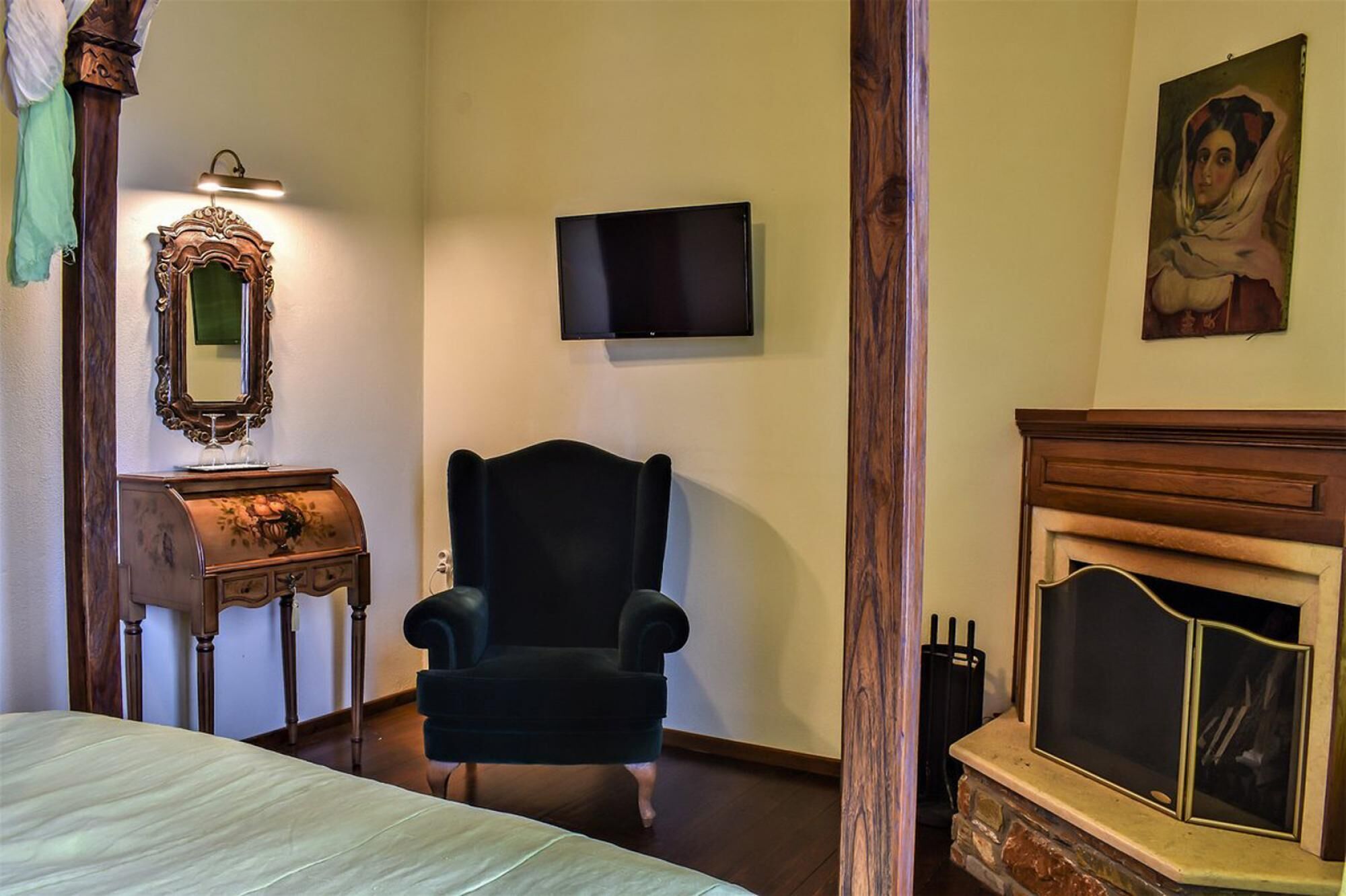 A bedroom with a bed, a chair, a television, a fireplace, and a mirror.