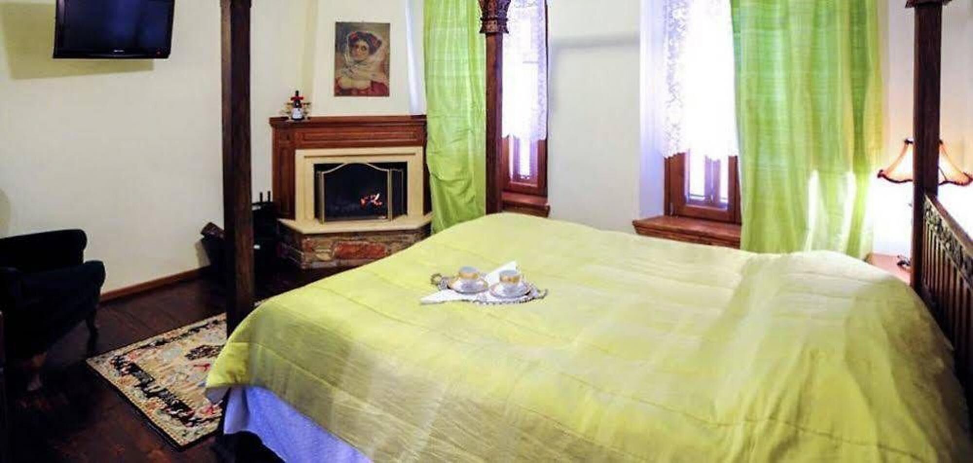 Une chambre à coucher avec un lit, une cheminée, un téléviseur et une fenêtre avec des rideaux.