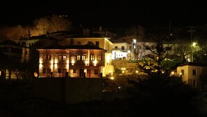 A multi-story building with stone facade and multiple windows, surrounded by other buildings and trees. - Archontiko Polyzos 11 Manolia (Volos)