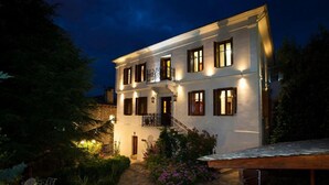 A two-story building with a stone pathway leading to the entrance, surrounded by greenery and a small outdoor seating area. - Archontiko Polyzos 11 Manolia (Volos)