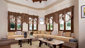 A cozy living room with a sectional sofa, two tables, and large windows with curtains. - Archontiko Polyzos 11 Manolia (Volos)