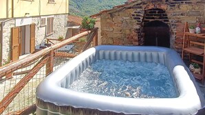 Une piscine gonflable installée à l’extérieur, entourée de bâtiments en pierre dotés de balcons en bois et d’un escalier menant à une porte.