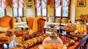Un bufé de desayuno con diversas opciones de comida, una zona de estar con sillas y un sofá, y una barra de madera con una vitrina de vidrio.