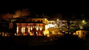 Vista nocturna de un edificio con múltiples ventanas y fachada de piedra, rodeado de otras construcciones y árboles.