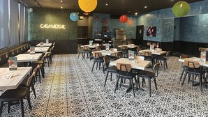 A restaurant with a black and white patterned floor, tables with chairs, and a neon sign reading "CASAMEZGAL".