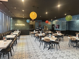 Restaurante com chão padronizado em preto e branco, mesas com cadeiras e um letreiro de neon que diz "CASAMEZGAL".
