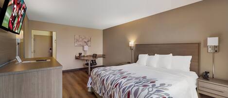 A hotel room with a bed, desk, and television.