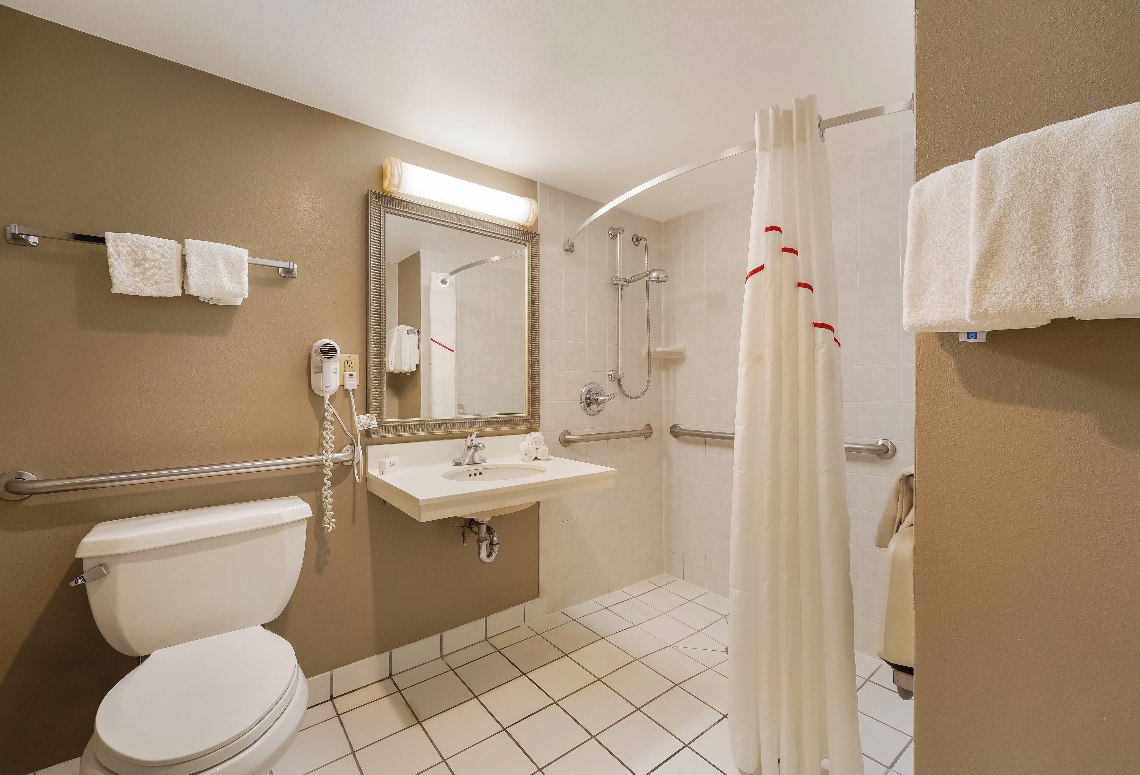 A bathroom with a toilet, sink, mirror, shower, and towel rack.