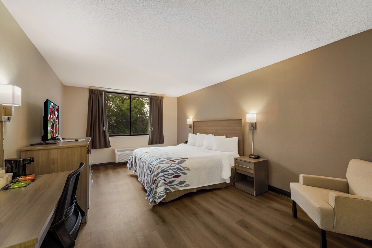 A hotel room with a bed, bedside tables, a desk, a chair, and a window with curtains.
