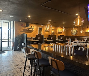 A restaurant interior with bar seating, pendant lighting, and decorative wall shelves.