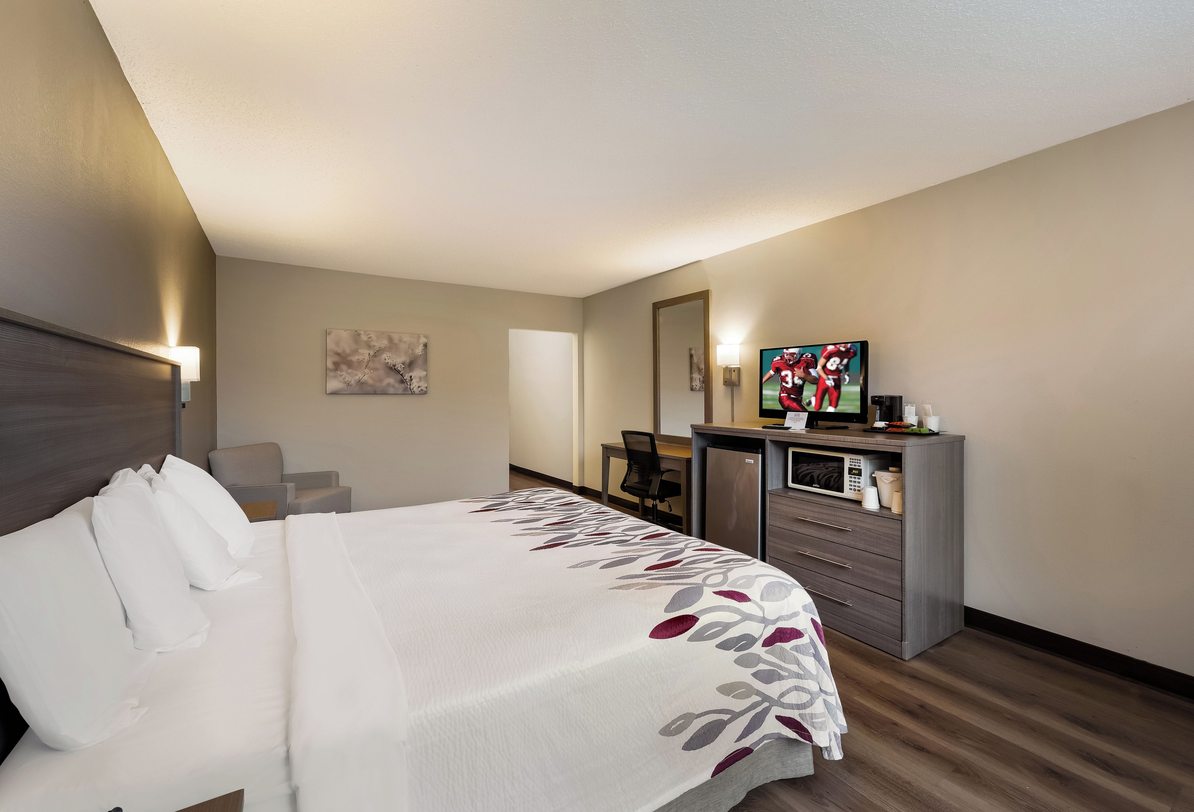 A hotel room with a bed, a desk, a television, and a refrigerator.