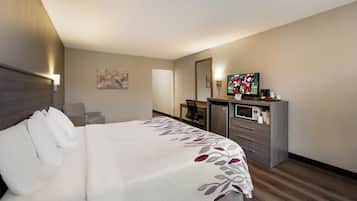Una habitación de hotel con cama, escritorio, televisor y refrigerador.