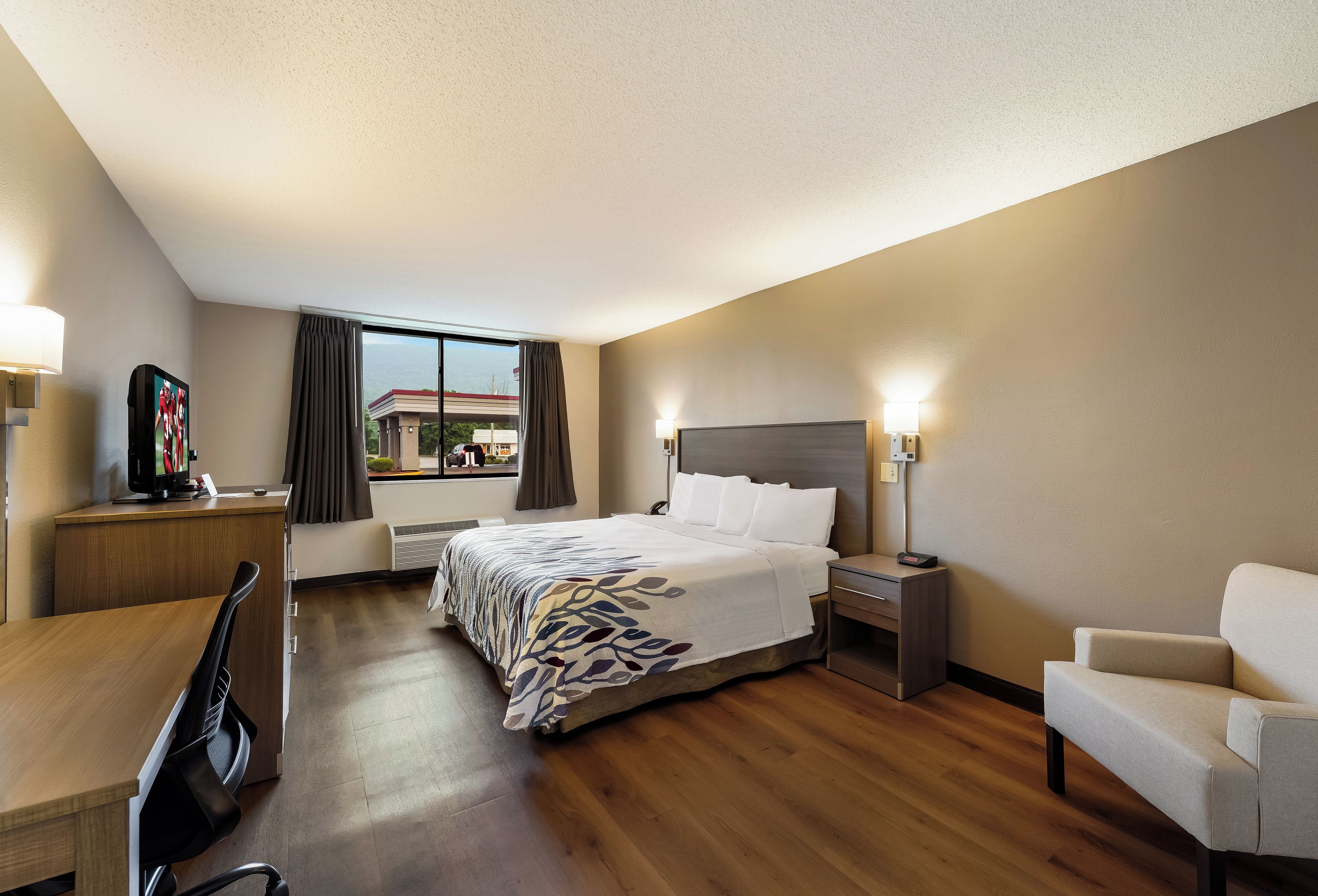 Una habitación de hotel con cama, mesitas de noche, escritorio, silla y televisor.