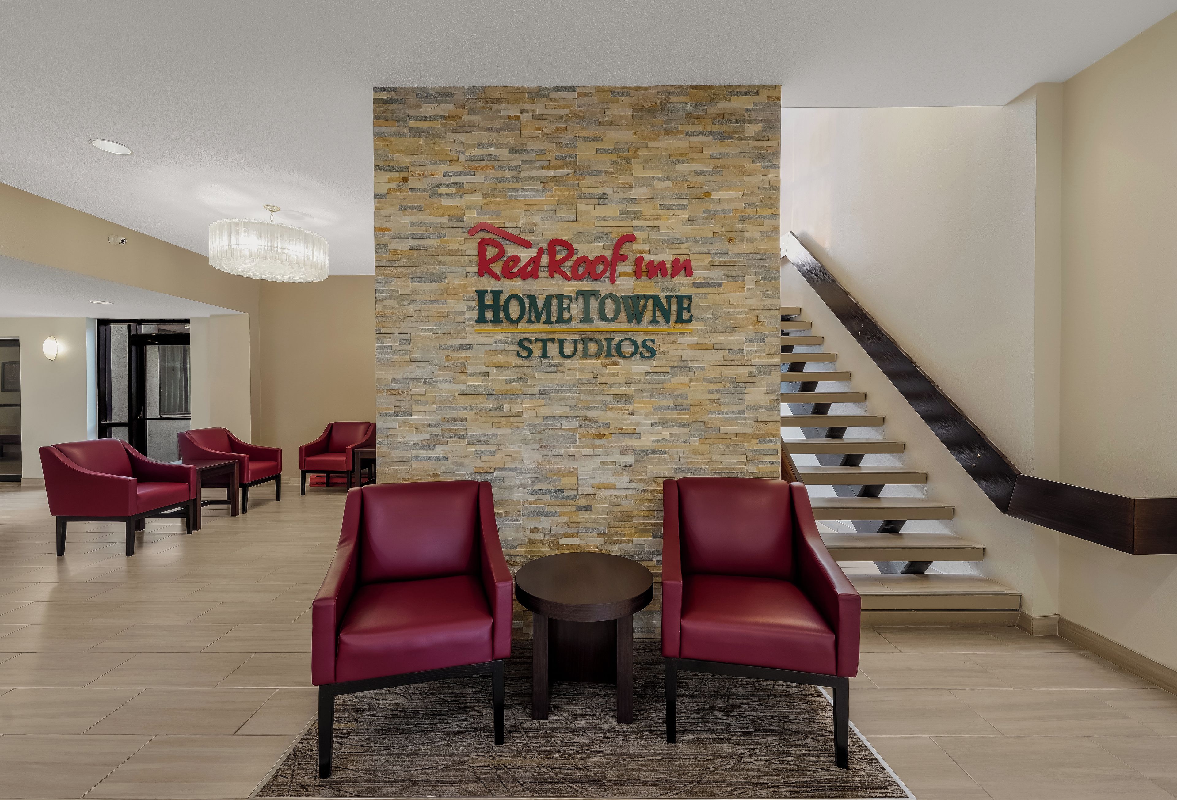 Le hall d’entrée d’un Red Roof Inn Hometown Studios, avec un mur en pierre, des fauteuils en cuir rouge, une petite table et un escalier.