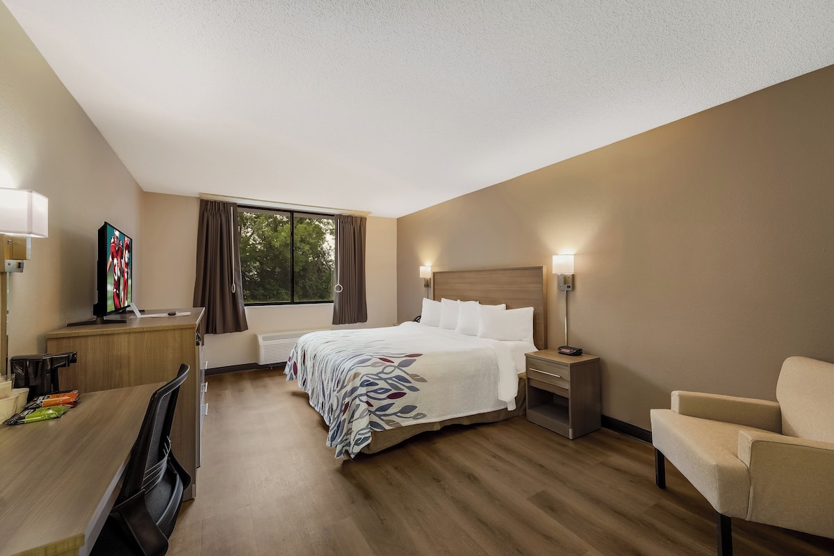 A hotel room with a bed, bedside tables, a desk, a chair, and a window with curtains.