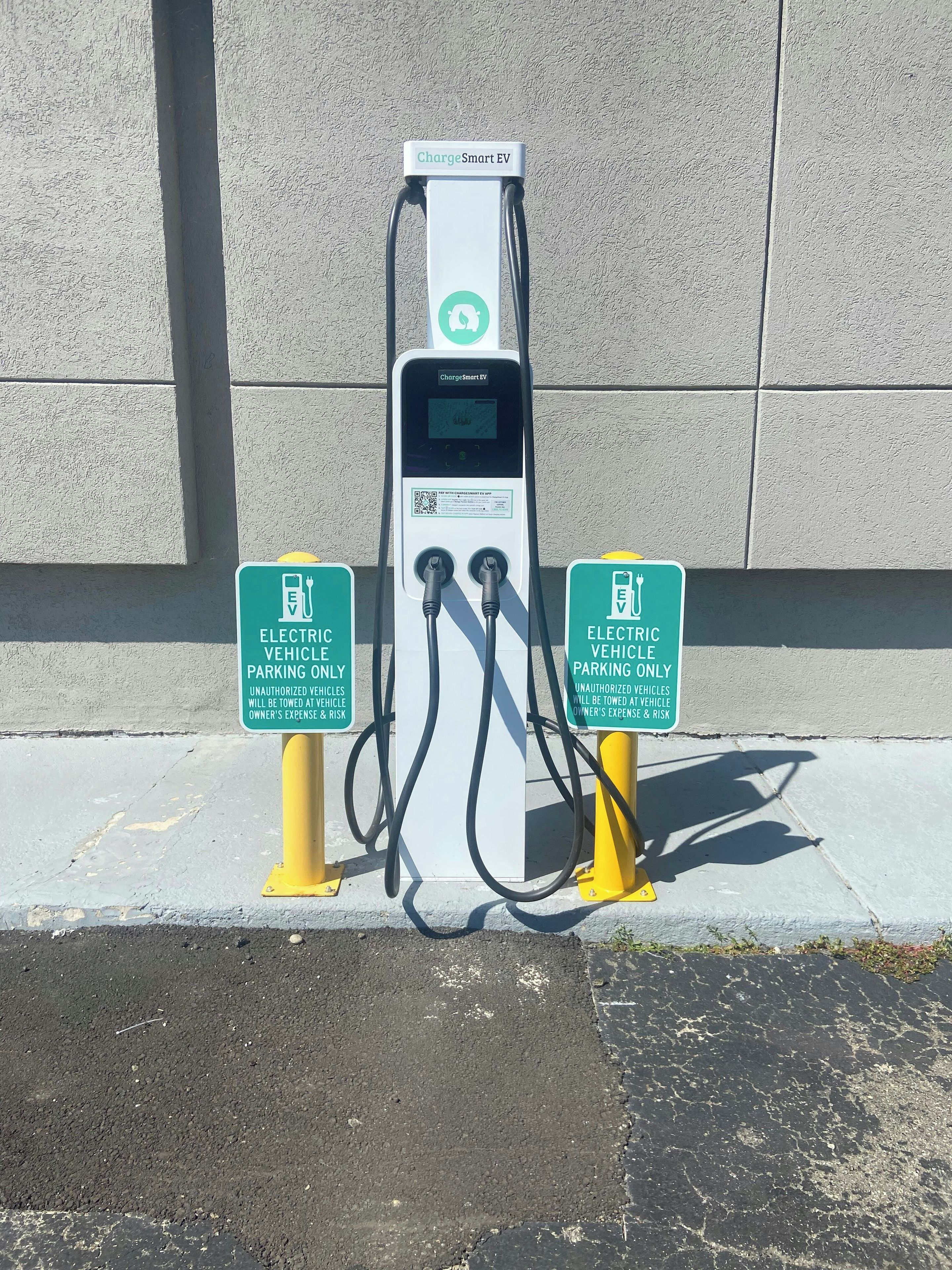 A ChargeSmart EV charging station with two yellow poles and two green signs indicating electric vehicle parking only.