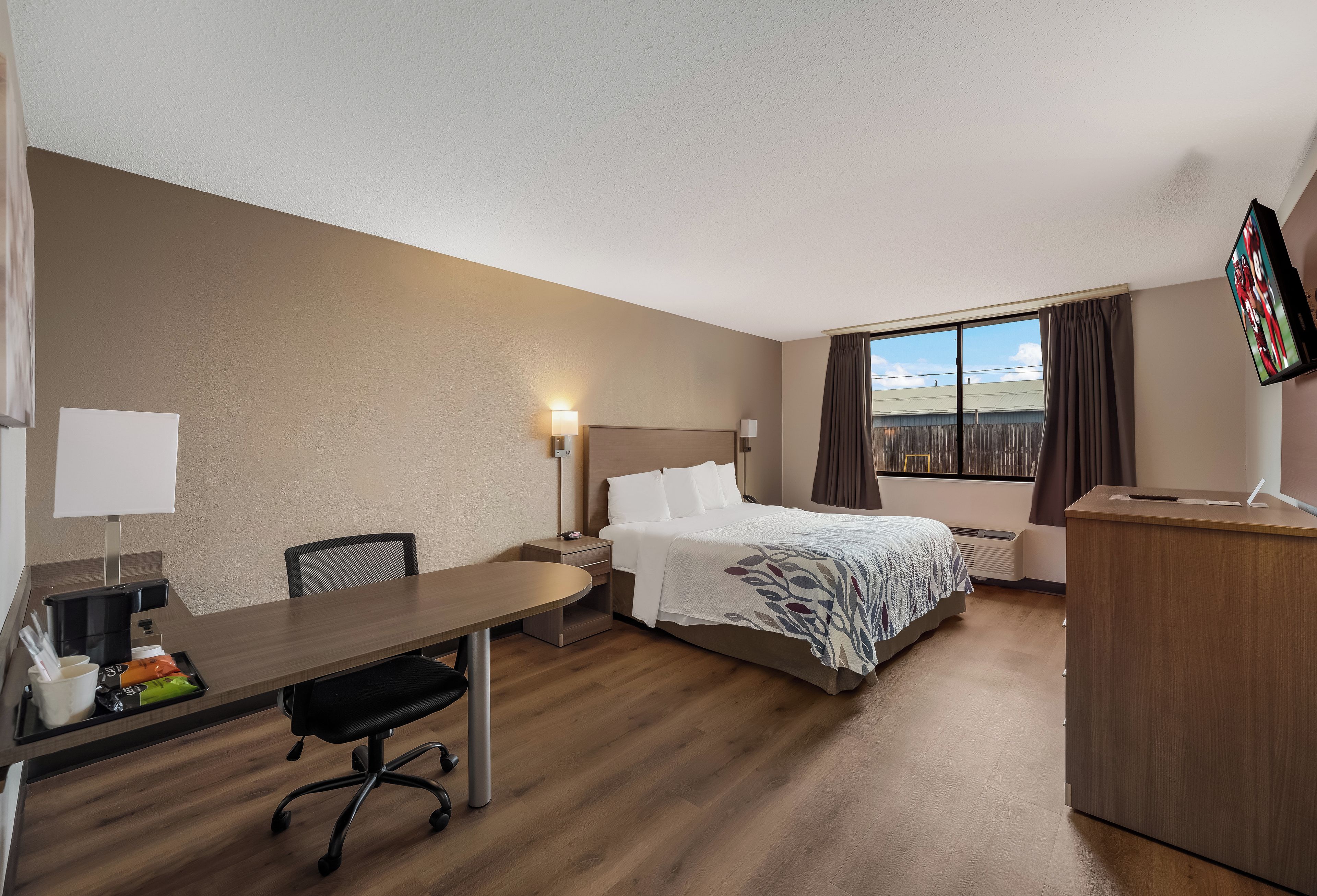 A hotel room with a bed, desk, chair, and a TV.