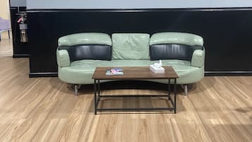 A green leather sofa with a wooden coffee table in front, against a dark wall and wooden floor.