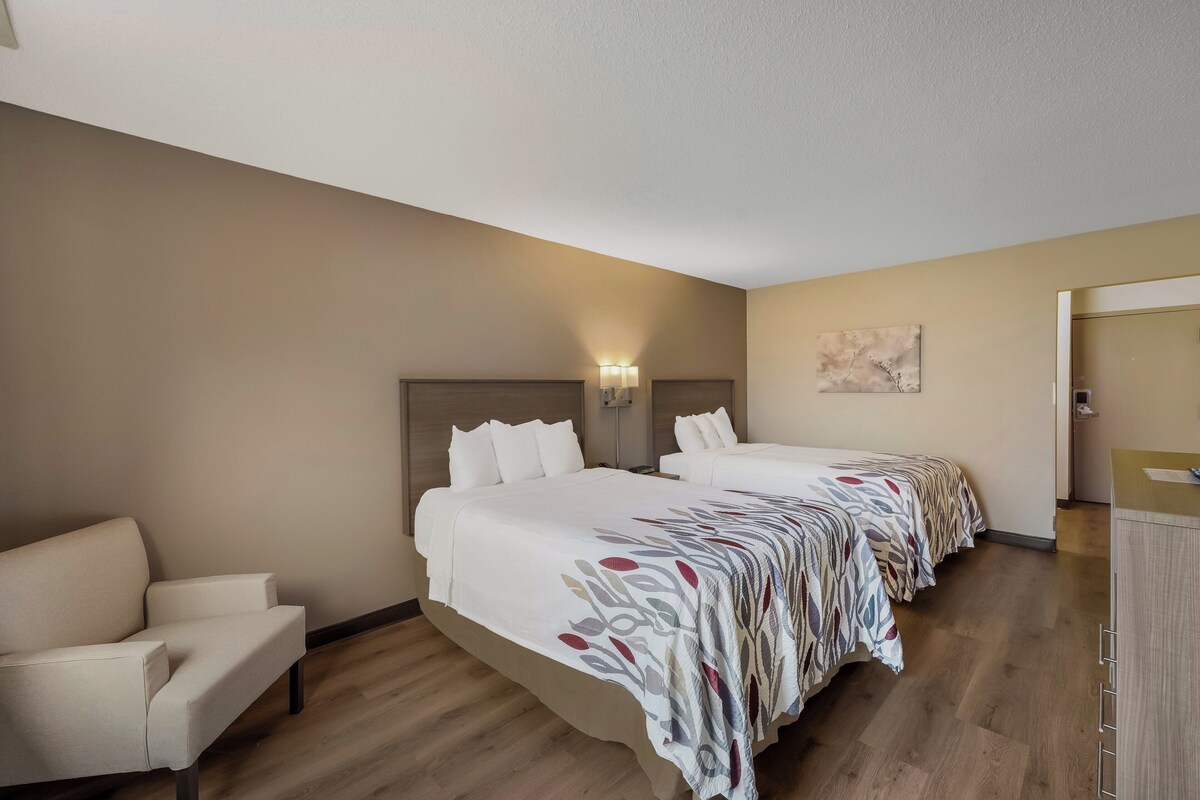 A hotel room with two beds, a sofa, a desk, and a painting on the wall.