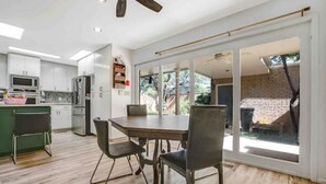A modern kitchen with white cabinets, a dining table with chairs, and a sliding glass door leading to a backyard. - Luxurious Tree House (Lubbock)