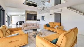 Een ruime woonkamer met een hoge plafond, een grote televisie en een kroonluchter.