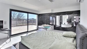 Een moderne slaapkamer met een groot bed, een badkuip, en een badkamer met een wastafel en spiegel.