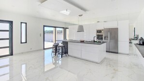 Een moderne keuken met een groot eiland, roestvrijstalen apparatuur en een glazen deur die naar een terras leidt.