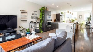 Una sala de estar moderna con sofá, mesa de centro y televisor. Se ve una cocina al fondo con una zona de comedor.