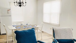 Una stanza con un tavolo da pranzo, due sedie imbottite blu, un lampadario e pareti bianche.