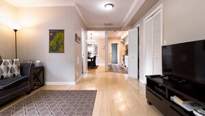A modern living room with a sofa, TV, and a patterned rug. A dining area is visible in the background. - Gray Corner Place | Walk Score 90 | Sleeps 9 (Washington)