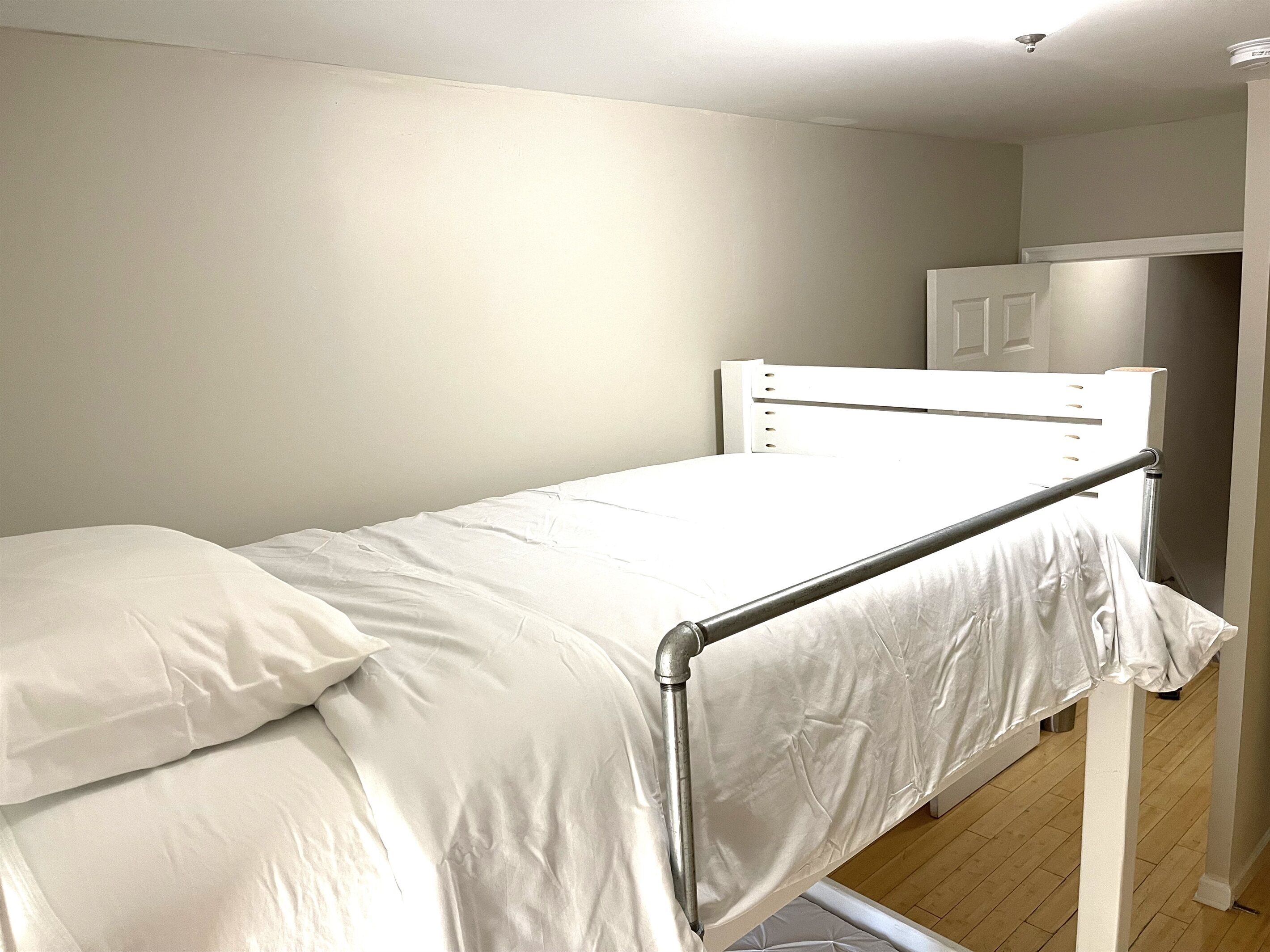A single bed with a metal frame and white bedding in a room with plain walls and a wooden floor.