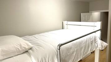 A single bed with a metal frame and white bedding in a room with plain walls and a wooden floor.
