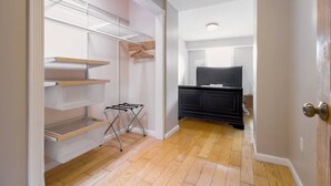A narrow hallway with a wooden floor, a black cabinet, and a white shelf unit with hanging clothes racks. - Gray Place | Walk Score 90 | Sleeps 12 (Washington)
