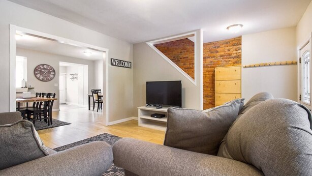 A modern living room with a grey sofa, a TV on a stand, and a 'WELCOME' sign. - Gray Place | Walk Score 90 | Sleeps 12 (Washington)