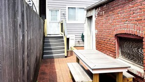 A narrow outdoor space with a wooden bench, a brick wall, and a wooden staircase leading to a door. - Gray Place | Walk Score 90 | Sleeps 12 (Washington)