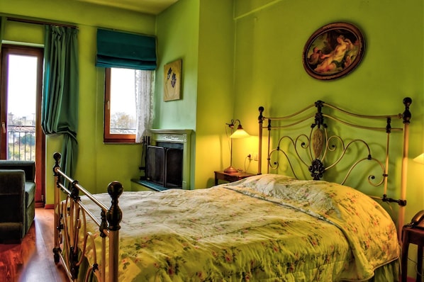 Una habitación con cama, escritorio, silla, ventana con cortinas, un cuadro en la pared y una lámpara en la mesita de noche.