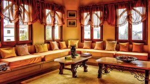 A cozy room with a large sofa, a coffee table, and a view of the outside through large windows with curtains. - Archontiko Polyzos 13 Menda (Volos)