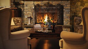 A cozy room with a stone fireplace, two armchairs, a wooden coffee table, and a vase with flowers. - Archontiko Polyzos 13 Menda (Volos)