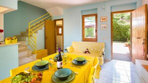 A dining area with a table set for two, a staircase, and a view of the garden through a window.