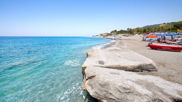 A beach with clear turquoise water, large rocks, and a row of beach umbrellas.