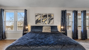A bedroom with a large bed, two windows, and three abstract paintings on the wall. - Game Themed, sleeps 12, king beds, walking distance to downtown & splash pad! (Harrison)