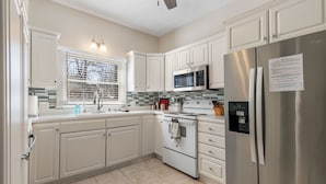 A modern kitchen with white cabinets, stainless steel appliances, and a window with blinds. - Game Themed, sleeps 12, king beds, walking distance to downtown & splash pad! (Harrison)